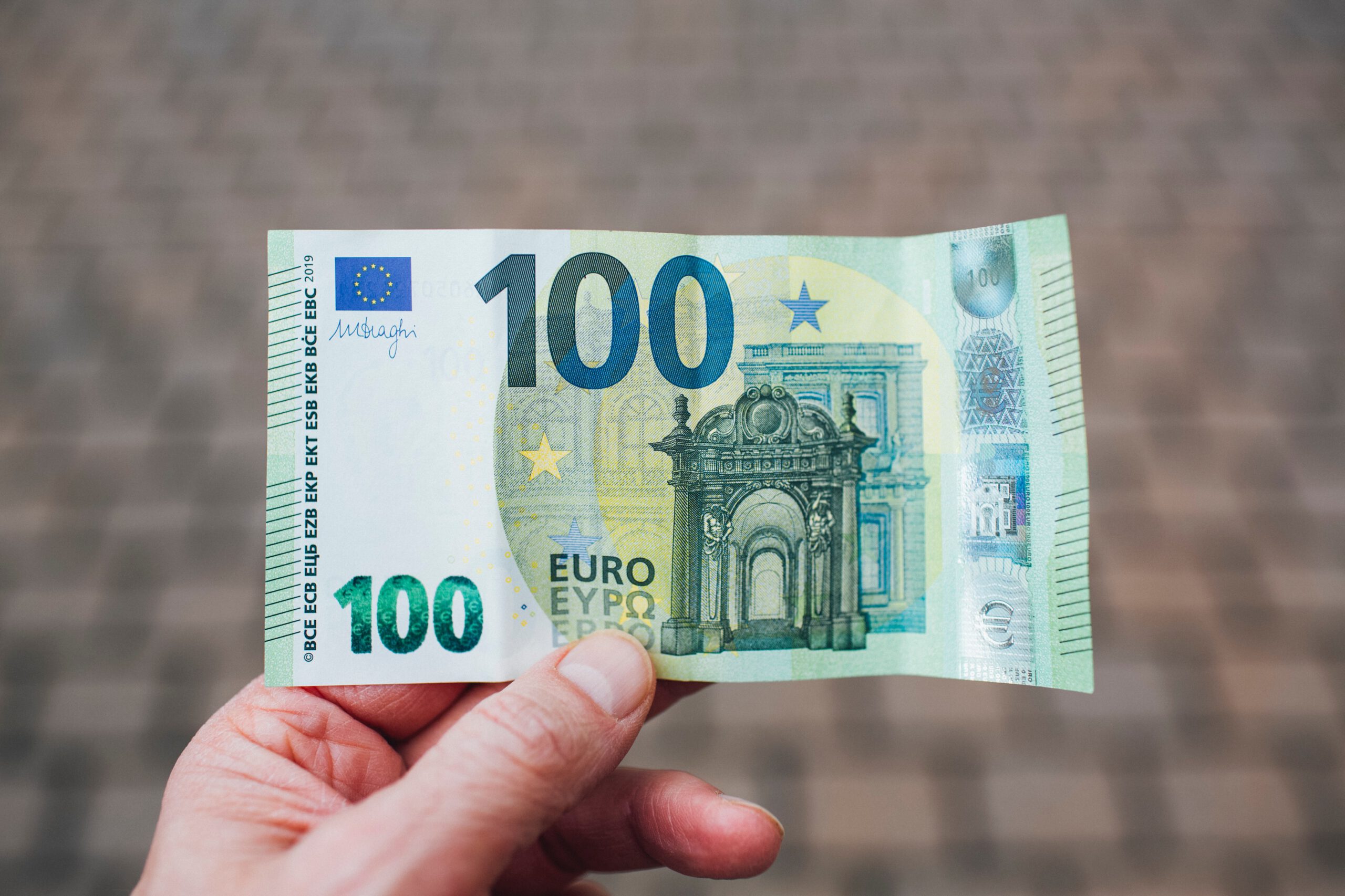 Dłoń trzymająca banknot stu euro na tle chodnika przy ulicy